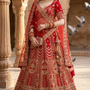 Bride in crimson red bridal lehenga with gold embroidery, standing in a heritage courtyard
