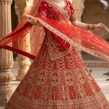 Bride twirling in crimson red bridal lehenga, dupatta flowing with gold embroidered skirt.