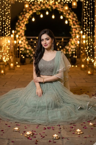 Woman seated in dusty mint lehenga surrounded by candles and petals