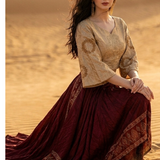 Woman seated in wine and beige fusion skirt set on desert sand