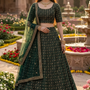 Woman in deep emerald green embroidered lehenga, garden courtyard backdrop
