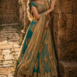Bride in rama green and gold embroidered lehenga with net dupatta, leaning against stone archway