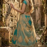 Bride in rama green and gold embroidered lehenga with net dupatta, standing against a stone wall