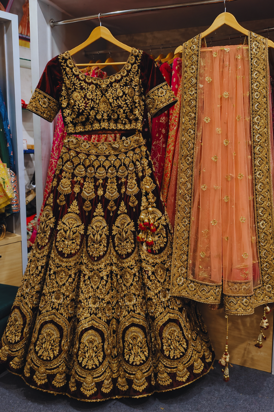 Maroon and peach bridal lehenga with gold embroidery, front view on display on hanger