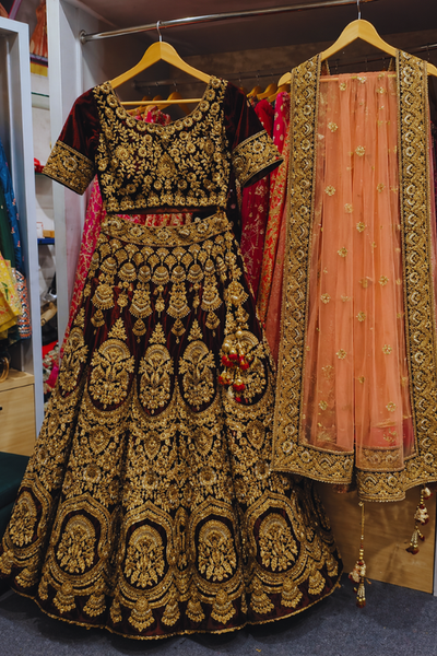 Maroon and peach bridal lehenga with gold embroidery, front view on display on hanger