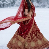 Bride in red bridal lehenga with dupatta flowing in the snow