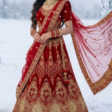 Bride in red velvet bridal lehenga with gold embroidery, standing in snow