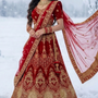 Bride in red velvet bridal lehenga with gold embroidery, standing in snow