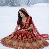 Bride seated in red velvet bridal lehenga with gold embroidery in the snow