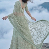 Sage green lehenga with dupatta spread wide, mountain cloud backdrop