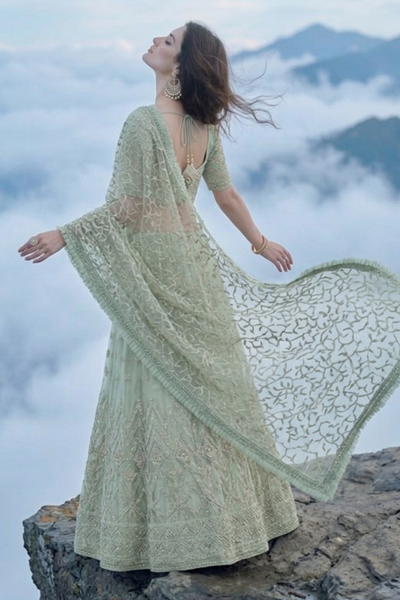 Sage green lehenga with dupatta spread wide, mountain cloud backdrop