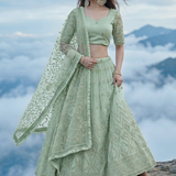 Woman in sage green embroidered lehenga, standing on a mountaintop above clouds