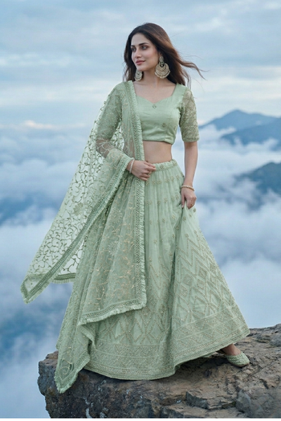 Woman in sage green embroidered lehenga, standing on a mountaintop above clouds