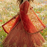 Bride in scarlet bridal lehenga with dupatta flowing in a wildflower field